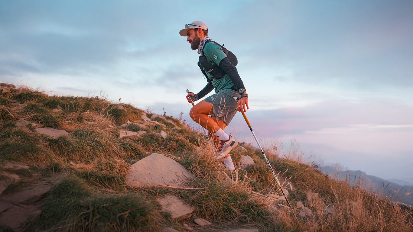 Traileur en montagne équipé de bâtons TSL, de chaussures Salomon et d'un t-shirt Millet.